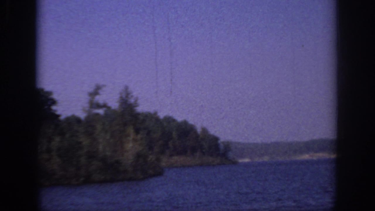 1966 Sacramento-area 8mm frame showing blue water, a tree-lined bank, distant shore, and visible film gate edges.