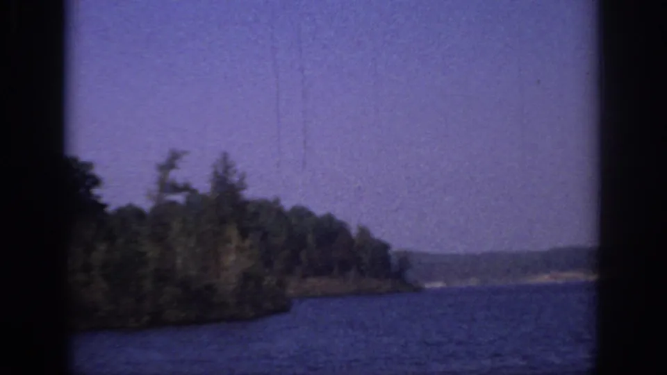 1966 Sacramento-area 8mm frame showing blue water, a tree-lined bank, distant shore, and visible film gate edges.