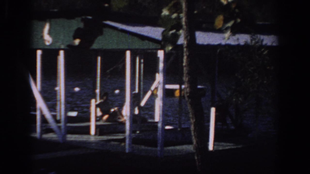 1966 Sacramento-area home-movie frame with a distant person seated on a covered dock above dark lake water.