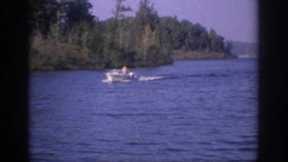 1966 Sacramento home-movie frame showing a small white motorboat moving across calm water near trees.