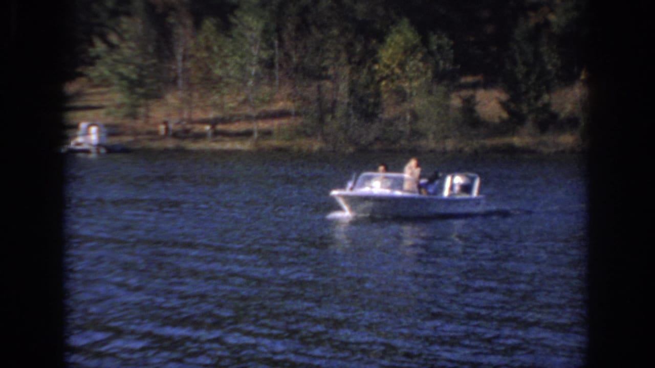 Small motorboat with passengers crossing a tree-lined lake.