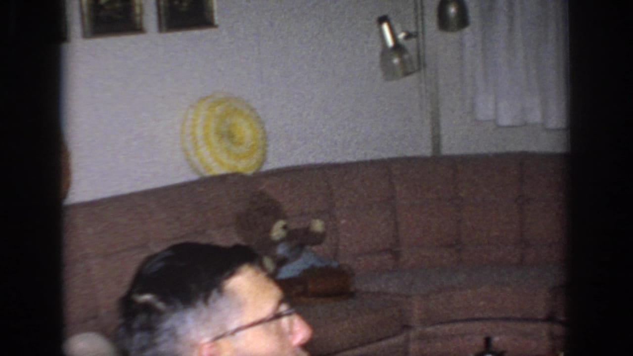 Brown sofa with yellow round pillow and partial view of a man with glasses in a living room.