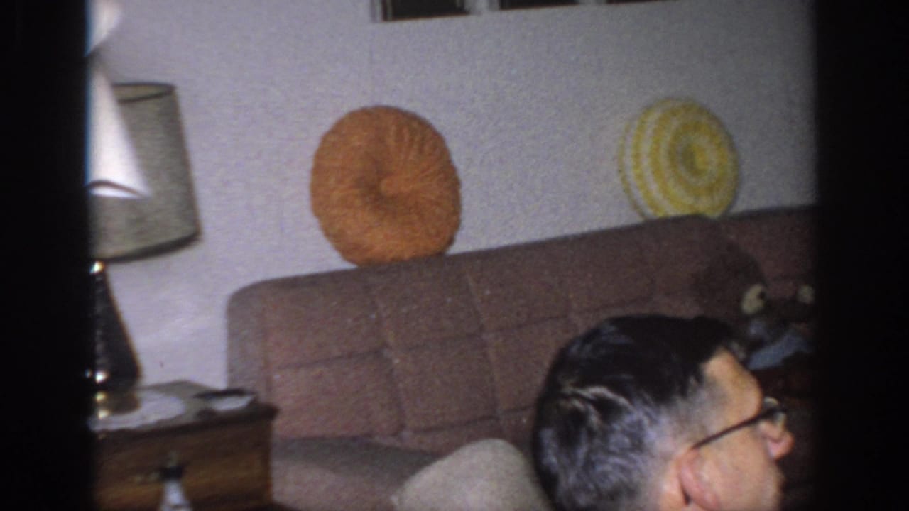 Living room sofa with orange and yellow round pillows, side table, lamp, and partial man in foreground.