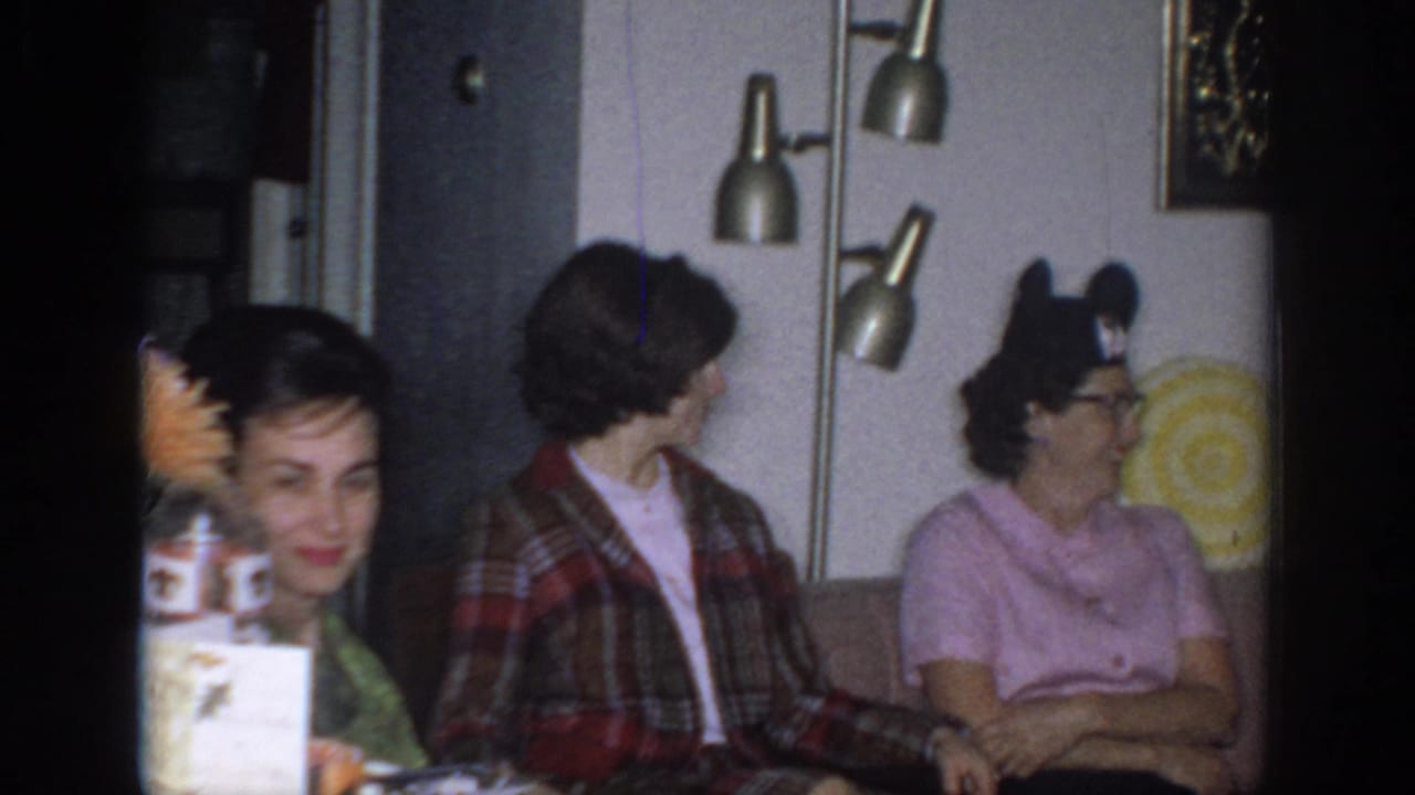 1966 Sacramento home-movie frame showing adult women seated in a private living room with mid-century decor and a floor lamp.