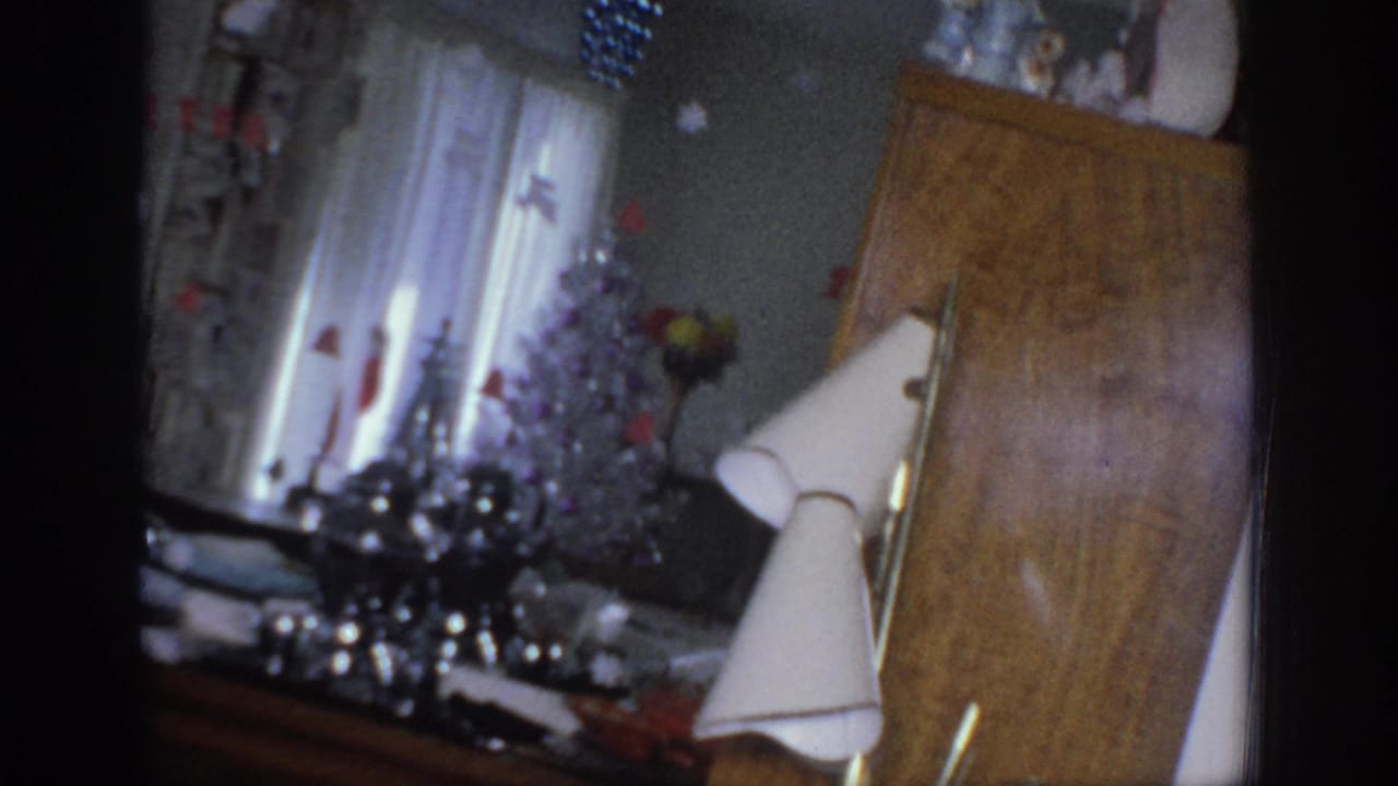 1966 Sacramento home-movie frame showing a decorated living room corner with curtains, tabletop holiday items, lamp, and cabinet.