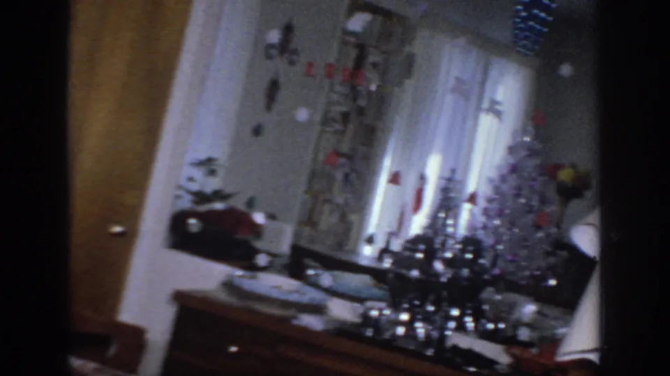 1966 Sacramento interior with white curtains, holiday tabletop decorations, lamp, and a silver tinsel tree during a slow pan.