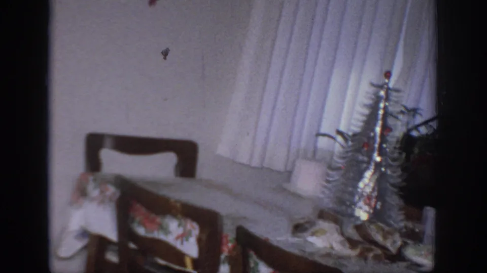 1966 Sacramento interior showing a silver tinsel tree by white curtains, with chairs, table covering, and holiday objects nearby.