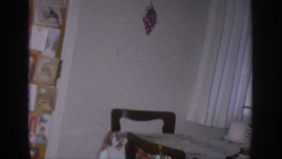 1966 Sacramento home-movie frame showing a domestic room corner with a chair, curtain, wall pictures, and partial holiday decor.