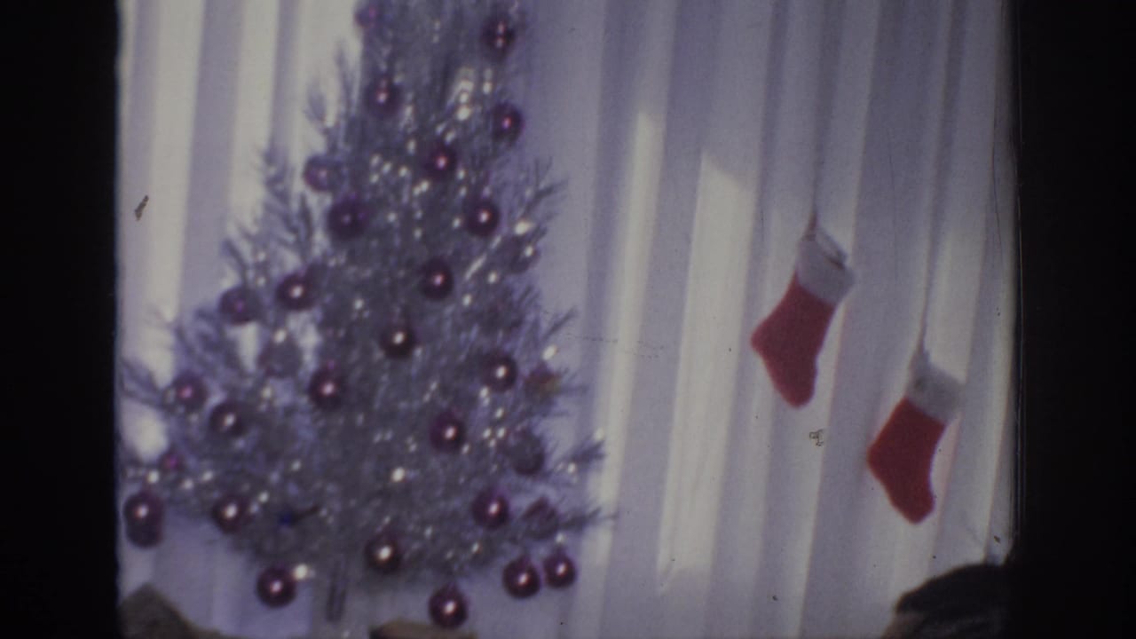 1966 Sacramento home-movie frame showing a silver Christmas tree, purple ornaments, white curtains, and hanging red stockings.