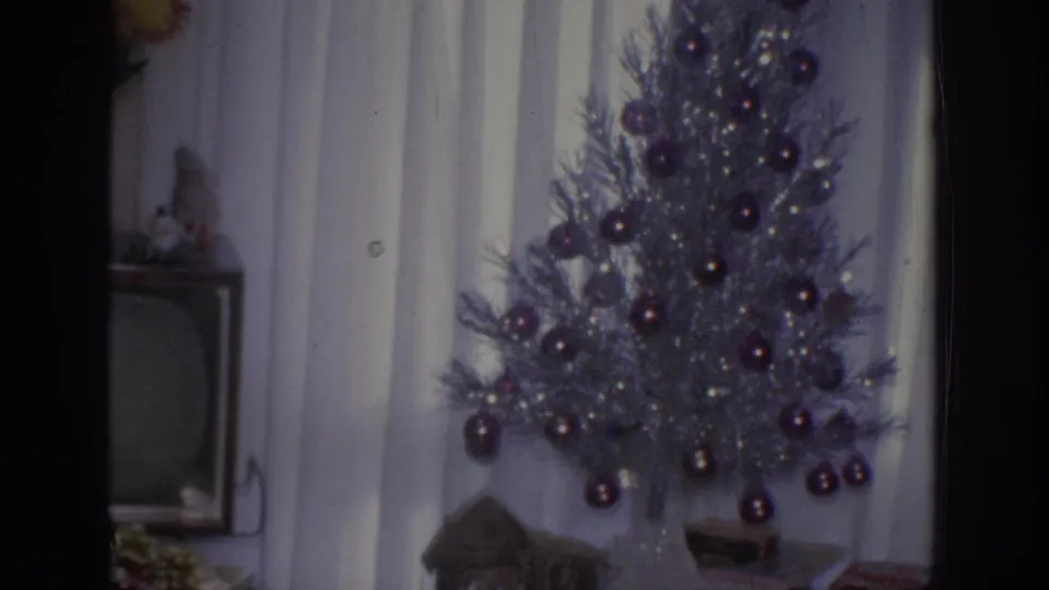 1966 Sacramento home-movie frame with a silver Christmas tree, purple ornaments, curtains, a television set, and a partial nativity display.