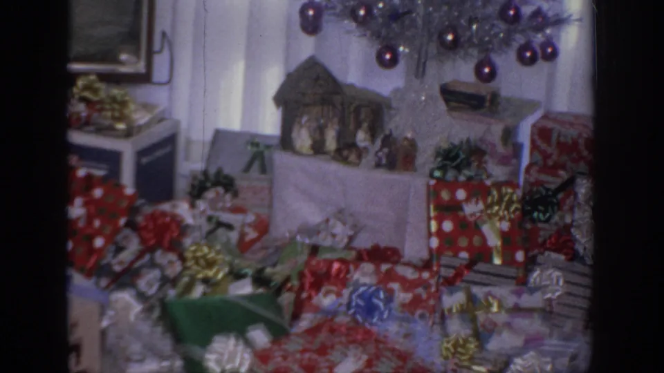 1966 Sacramento Christmas interior showing wrapped presents, shiny bows, a small nativity scene, and the lower branches of a silver tree.