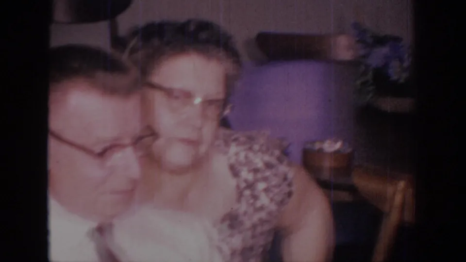 1966 Sacramento 8mm frame with two adults seated close together, partly soft and faded, in a private home interior.