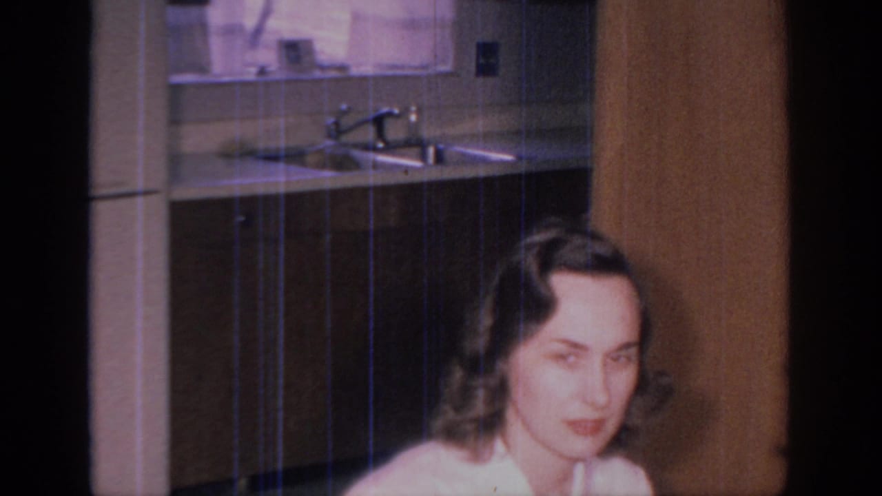 Woman faces partly toward the camera beside wood paneling and a kitchen sink area.