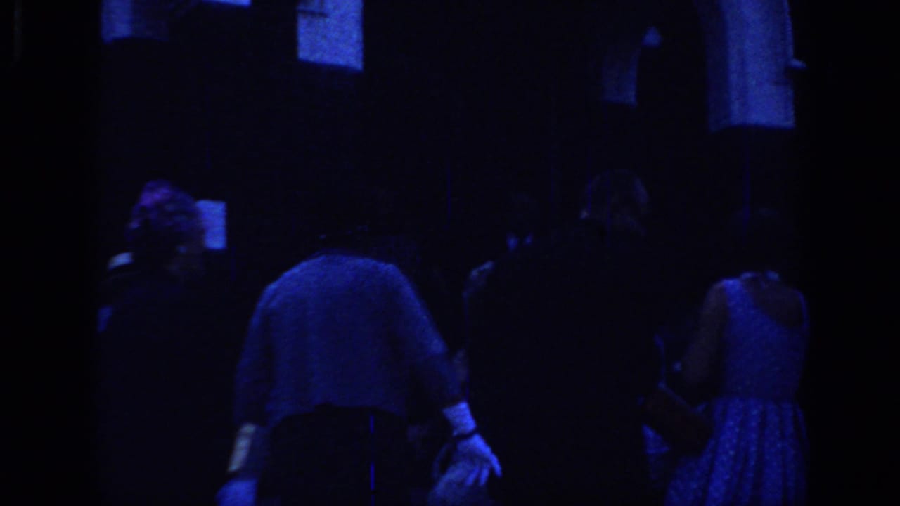 1966 Sacramento home-movie frame showing formally dressed adults mingling outside a dark building under strong blue color shift.