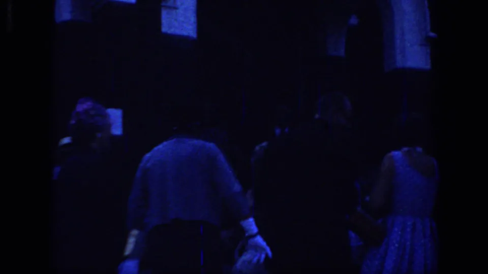 1966 Sacramento home-movie frame showing formally dressed adults mingling outside a dark building under strong blue color shift.