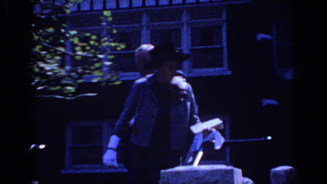In 1966 Sacramento home-movie footage, a formally dressed couple stands near a shaded house entry with windows and greenery behind them.