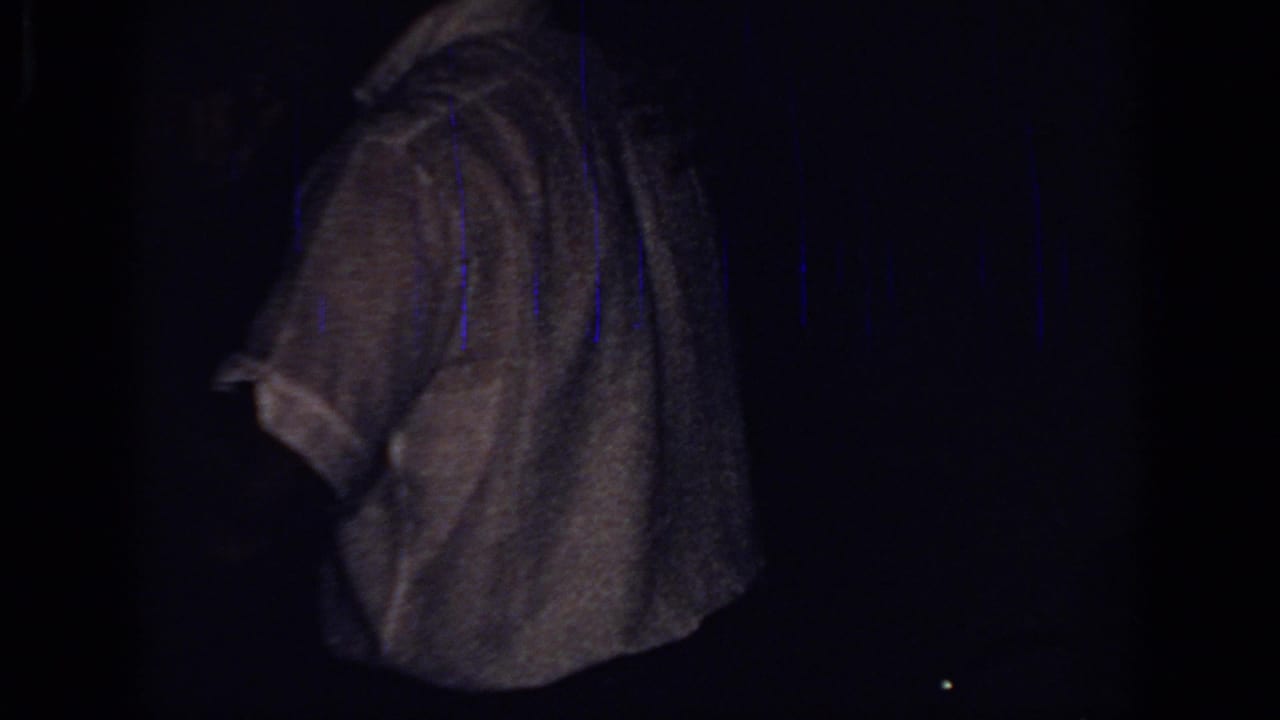 White-shirted figure turned away, isolated against a black low-light frame.