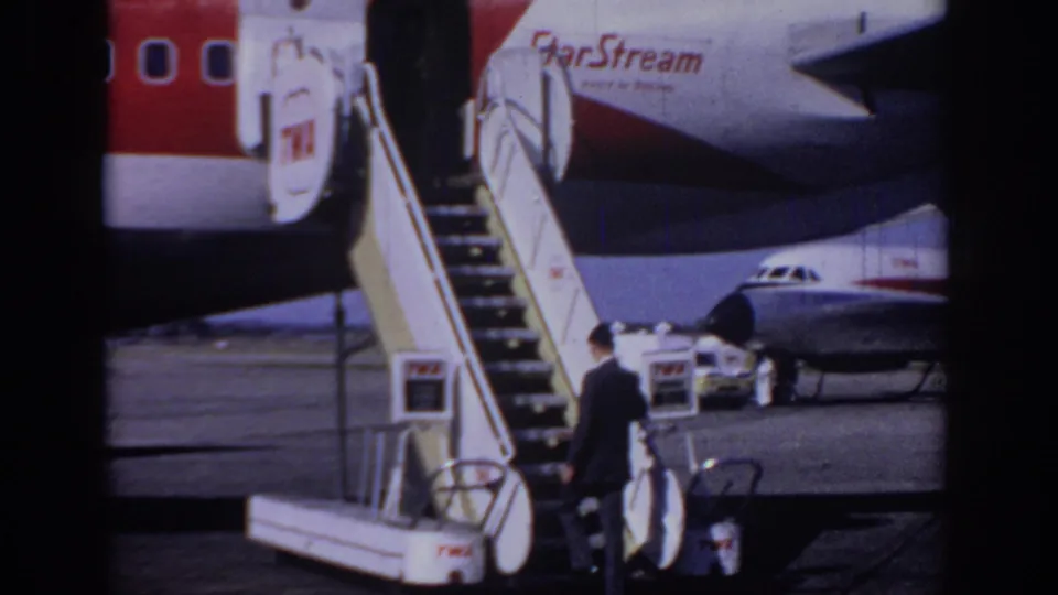Rear view of the suited passenger nearing the mobile stairs, with StarStream lettering and TWA colors visible on the aircraft.