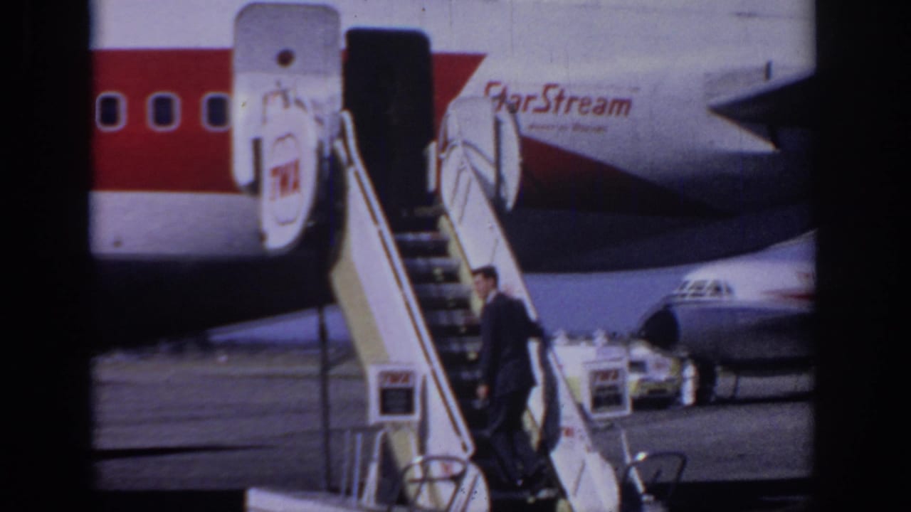 Man in a dark suit approaches mobile stairs beside a TWA StarStream aircraft.