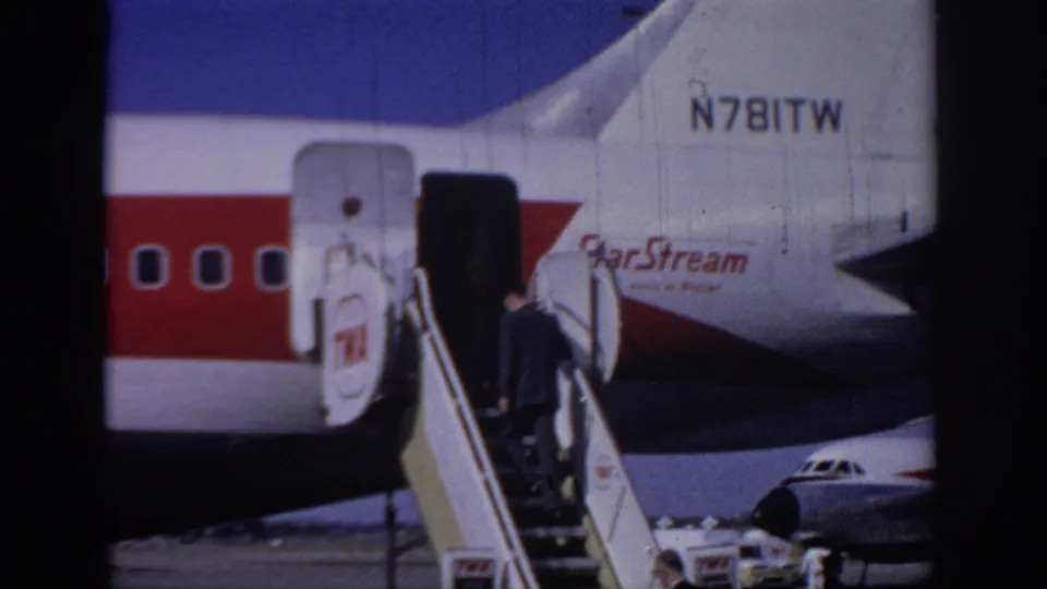 The passenger continues up the portable stairs toward the TWA StarStream aircraft door in this 1966 Sacramento airport home-movie frame.