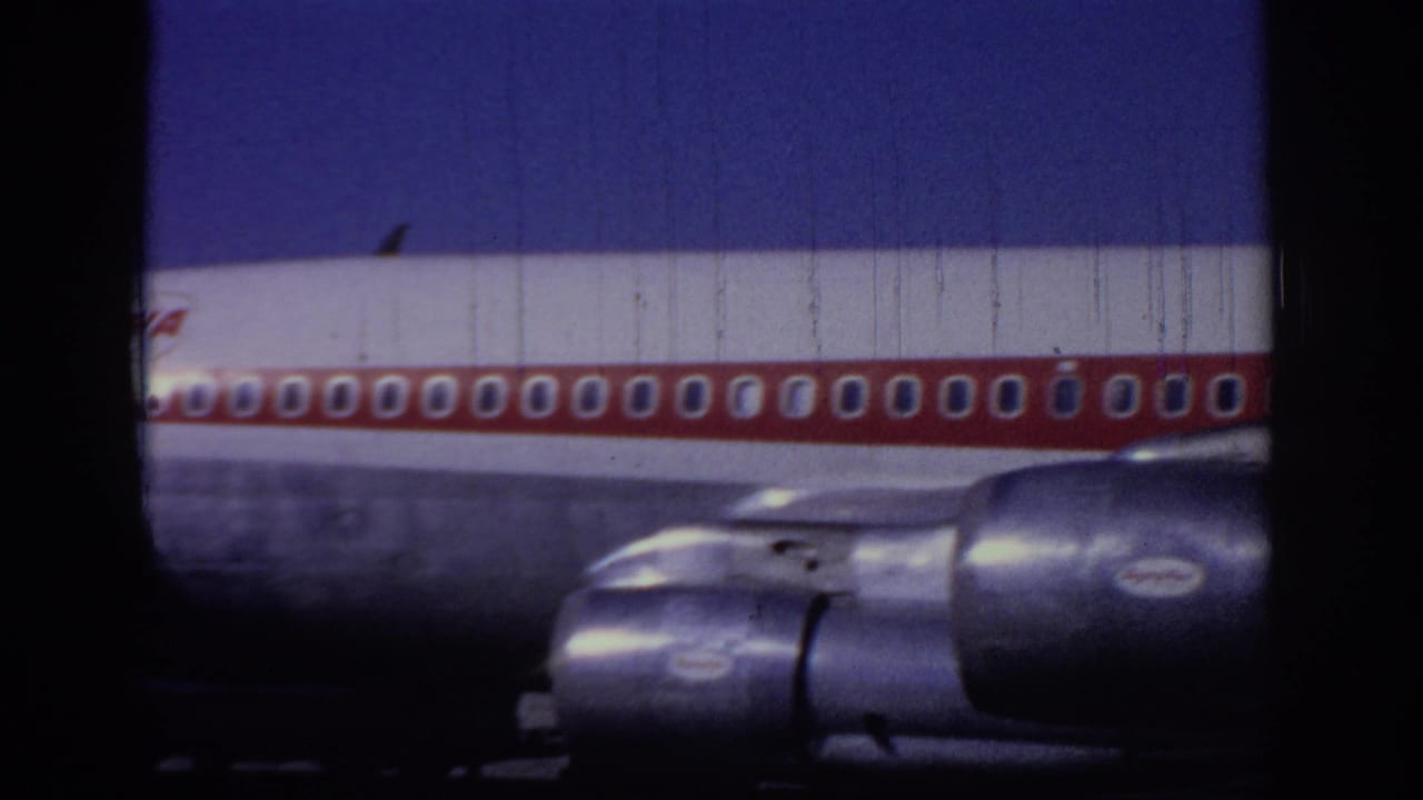 1966 Sacramento home-movie frame showing a close low-angle view of a TWA jet fuselage, red window stripe, and engines.