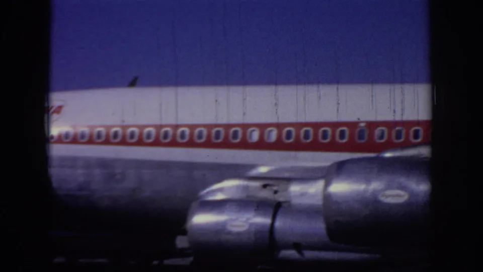 1966 Sacramento home-movie frame showing a close low-angle view of a TWA jet fuselage, red window stripe, and engines.