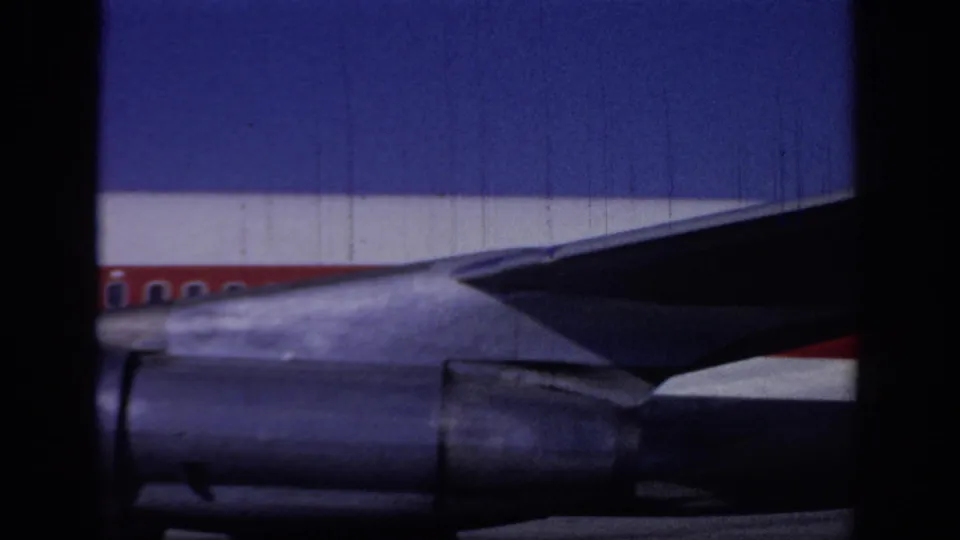 1966 Sacramento home-movie frame showing the underside of a TWA jet wing, engine nacelles, and red-striped fuselage.