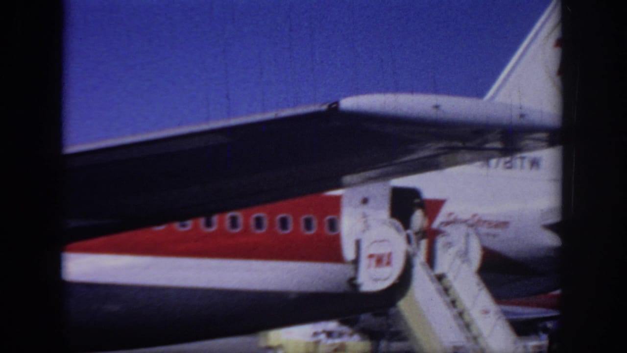 1966 Sacramento home-movie frame showing a close side view of a TWA airliner, mobile boarding stairs, and part of the tail.