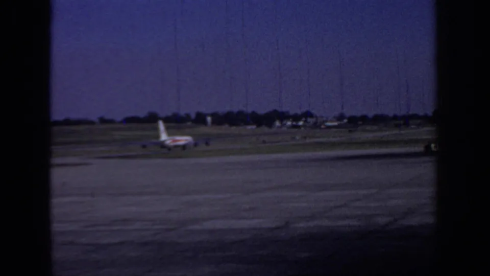 Wide 1966 Sacramento runway view showing a TWA aircraft at distance on the tarmac with airport structures along the horizon.