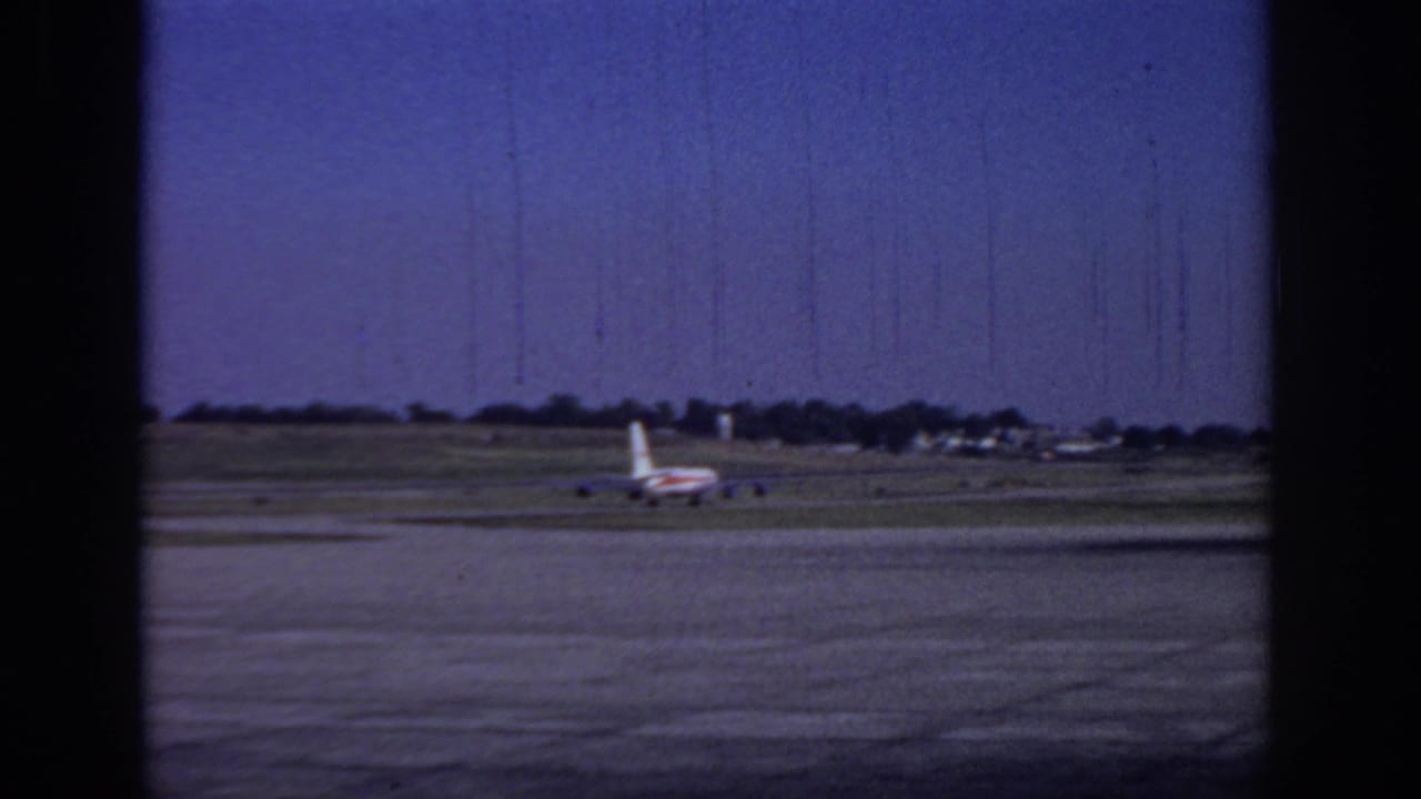 1966 Sacramento runway view with a commercial jet in the distance, grass airfield strips, blue sky, and visible 8mm film wear.