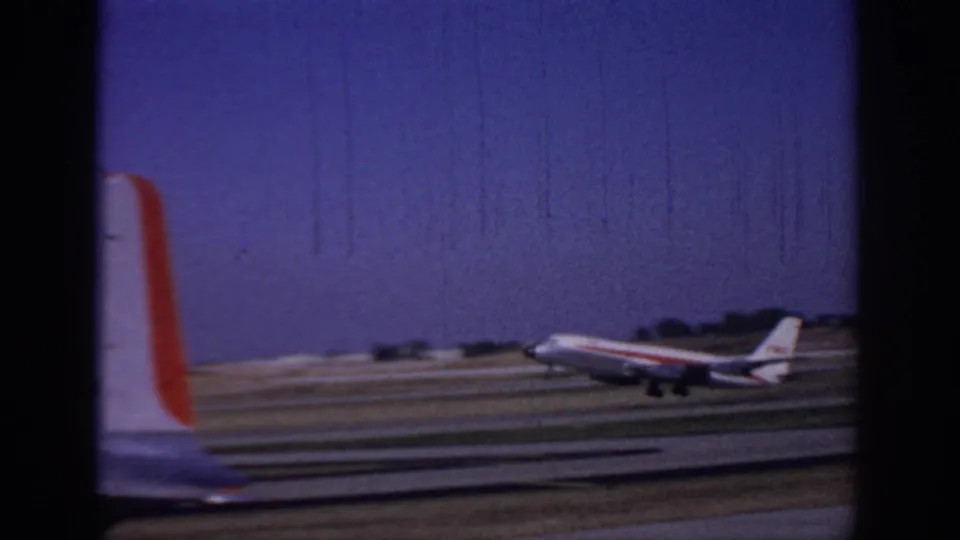 A commercial jet appears to lift or roll on the Sacramento runway while another aircraft tail passes in the foreground of the 8mm frame.