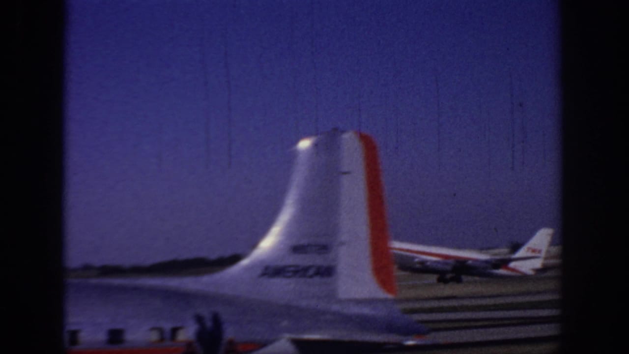 1966 Sacramento airport home-movie frame showing a TWA jet on the runway, partly obscured by another aircraft tail in the foreground.