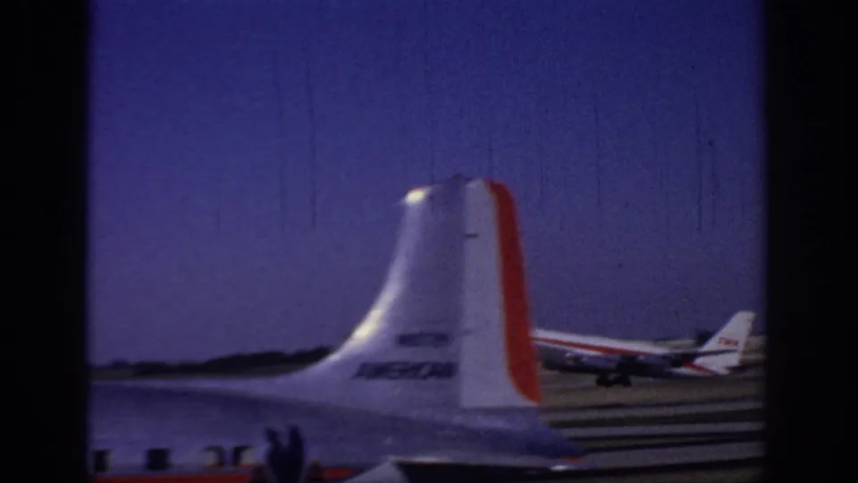 1966 Sacramento airport home-movie frame showing a TWA jet on the runway, partly obscured by another aircraft tail in the foreground.
