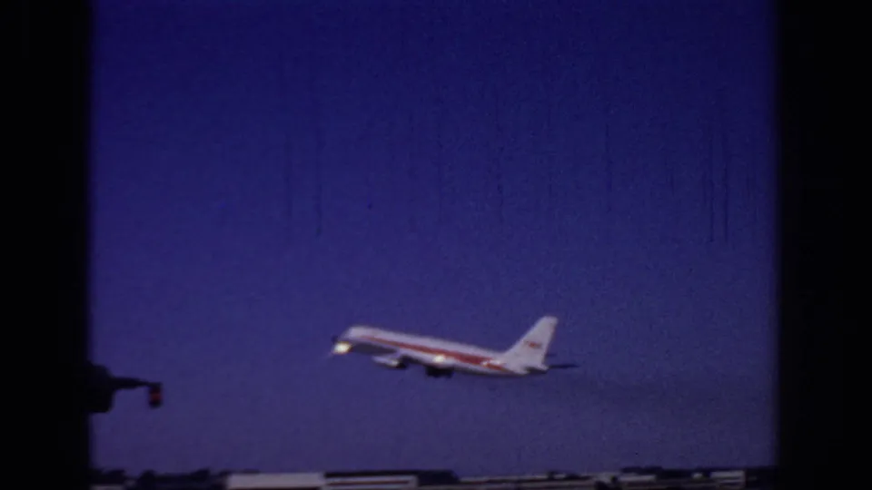 1966 Sacramento airport frame of a TWA jet climbing into a deep blue sky, with low airport structures along the bottom edge.