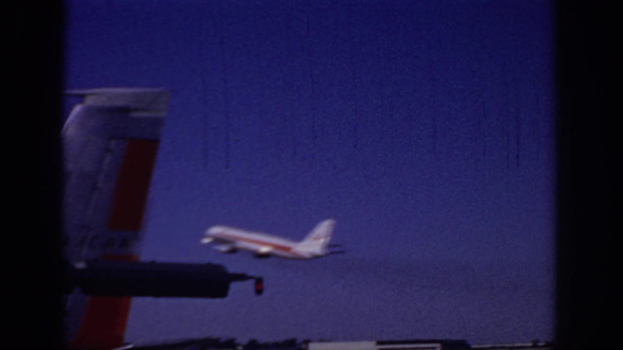 1966 Sacramento home-movie frame showing a passenger jet taking off against a deep blue sky, with a partial aircraft tail in the foreground.