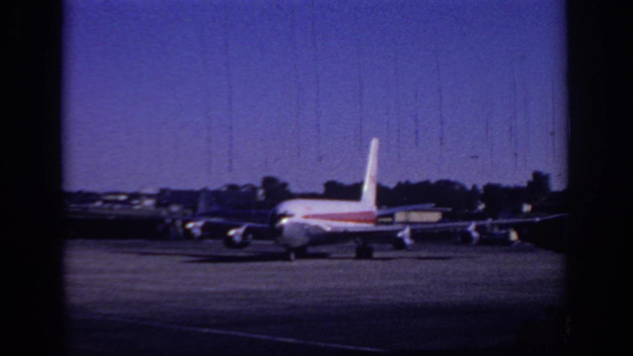 1966 Sacramento airport home-movie frame showing a TWA-style white jetliner with red stripe moving across the tarmac.