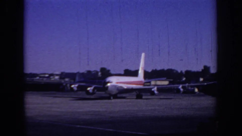 1966 Sacramento airport home-movie frame showing a TWA-style white jetliner with red stripe moving across the tarmac.
