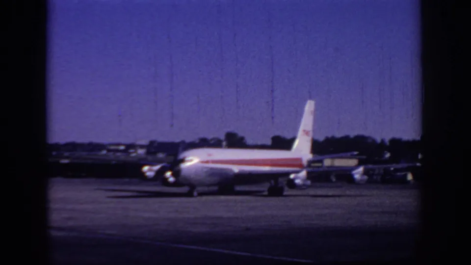 A closer 1966 home-movie view of the commercial jet taxiing on the Sacramento airport tarmac under blue sky.
