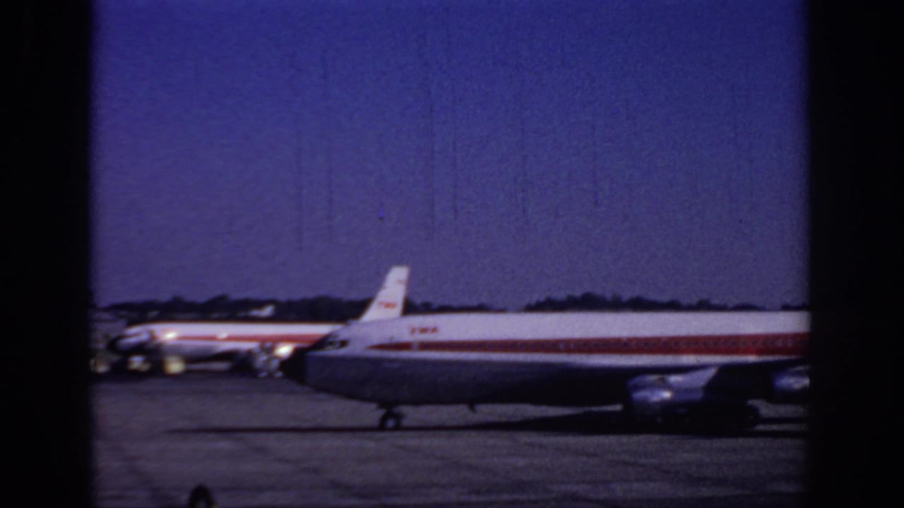 1966 Sacramento airport home-movie frame showing a red-and-white TWA passenger jet moving across the tarmac.