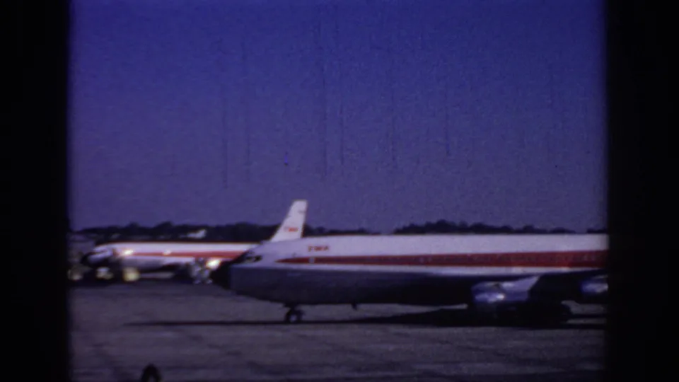 1966 Sacramento airport home-movie frame showing a red-and-white TWA passenger jet moving across the tarmac.