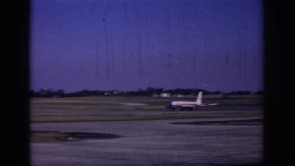 Wide 1966 Sacramento airport home-movie frame with a distant TWA jet taxiing across the runway area.