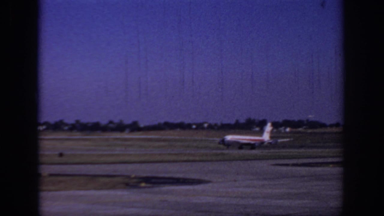 1966 Sacramento airport home-movie frame showing a commercial jet low on the runway beyond grass and pavement, with dark 8mm borders.