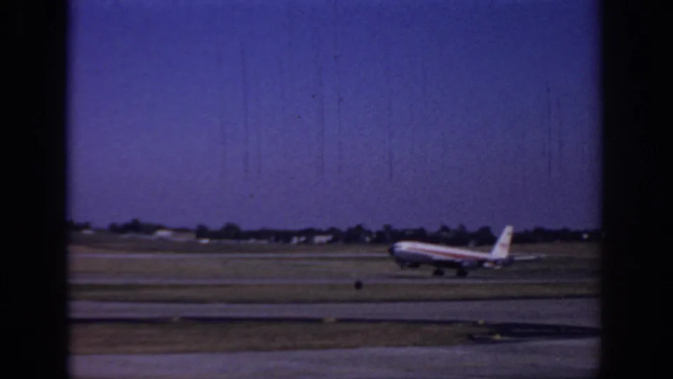 1966 Sacramento airport footage frame showing a striped commercial jet beginning its takeoff run or lift from the runway.