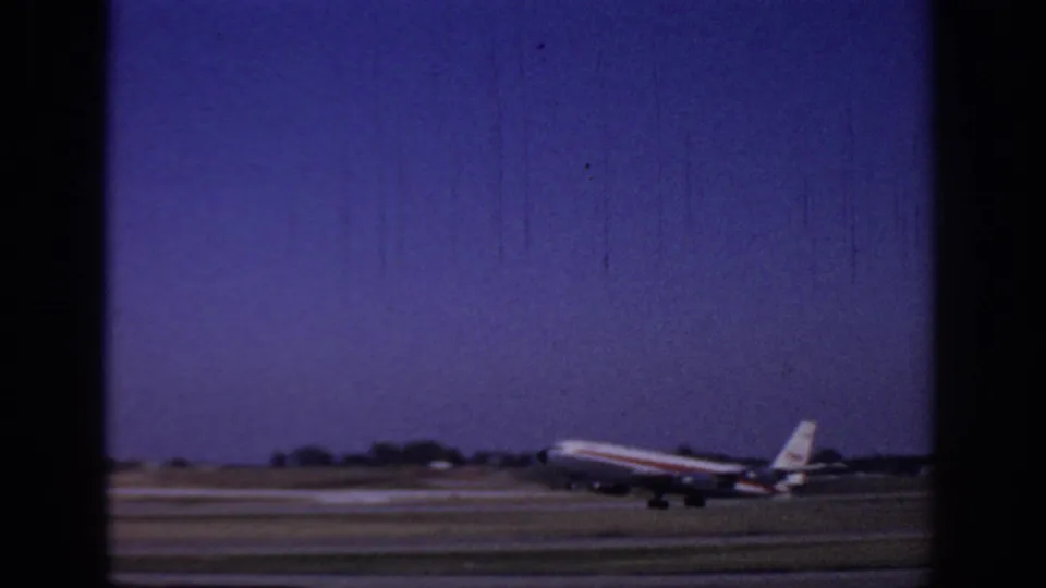 1966 Sacramento airport home-movie frame showing a commercial jet lifting low over the runway, with landing gear still visible.
