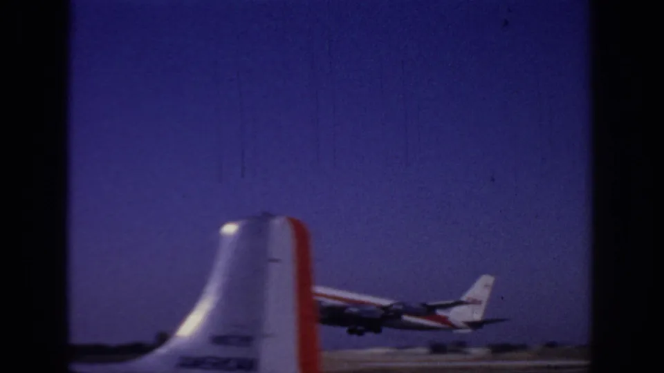 1966 Sacramento airport frame showing the jet climbing beyond a close foreground aircraft tail, with heavy 8mm grain and dark borders.