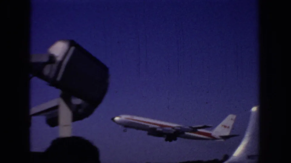 1966 Sacramento airport footage showing a TWA passenger plane climbing against a deep blue sky from a low home-movie angle.