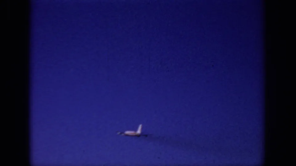 Distant small airplane over Sacramento sky in 1966 home-movie footage, with a faint smoke or vapor trail and visible 8mm grain.