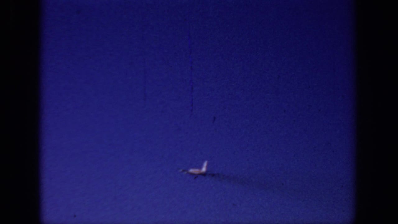 Small airplane farther across a blue sky, leaving a thin dark trail.
