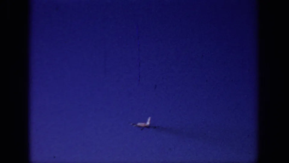 Small distant aircraft moves across the blue Sacramento sky in 1966 footage, with soft 8mm texture and a faint trail behind it.