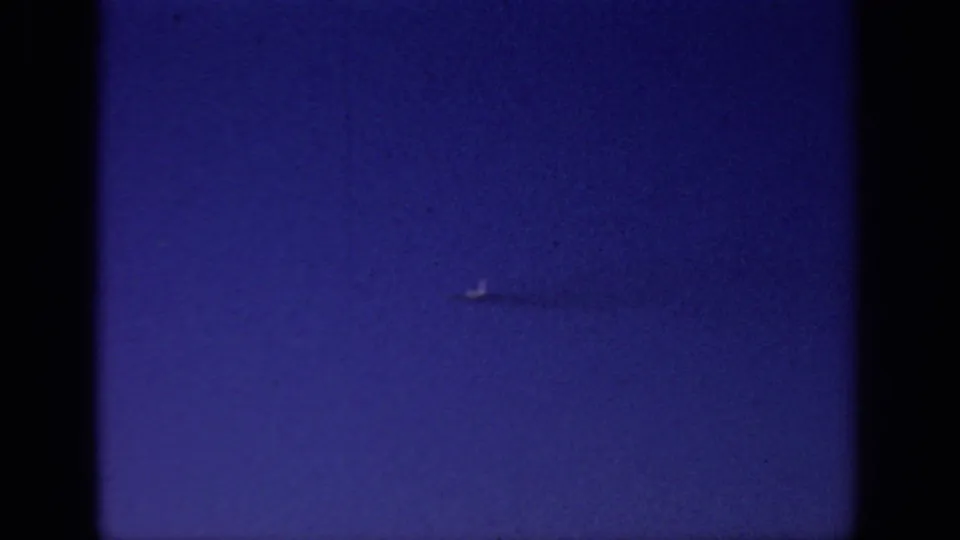 1966 Sacramento 8mm frame showing a small distant flying object against blue sky, with grain and dark film borders.